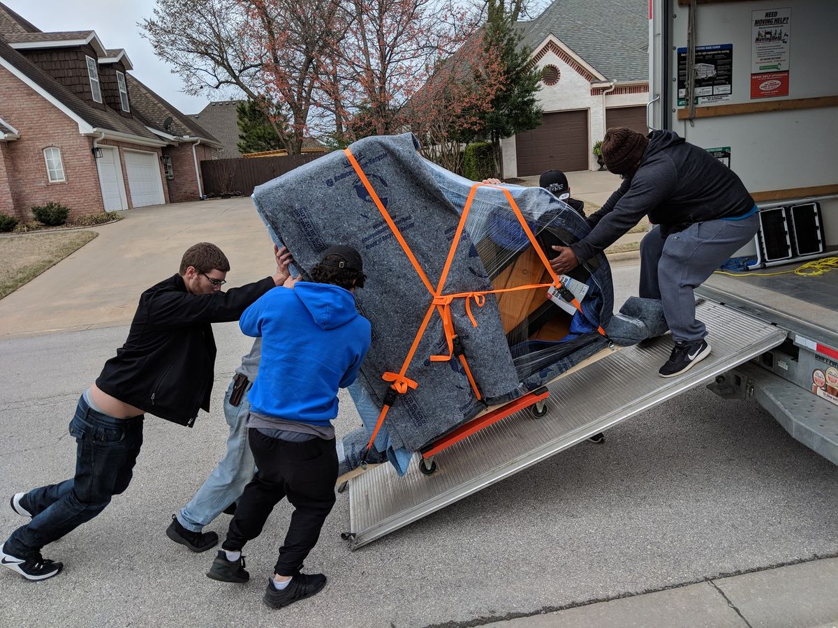 Movers straining to push a heavy piano up a truck ramp